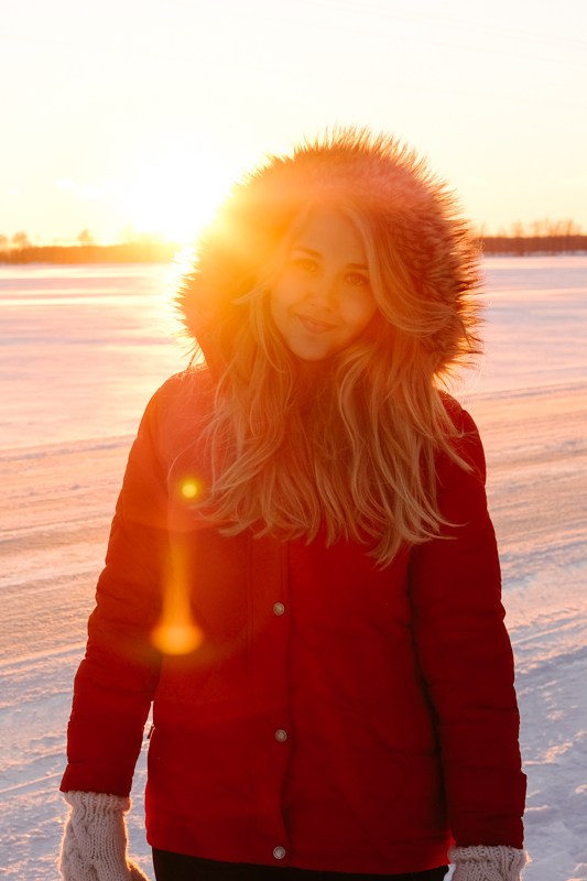 Debora Dahl wearing a red coat in the snow with the sunset behind her monalisa smile
